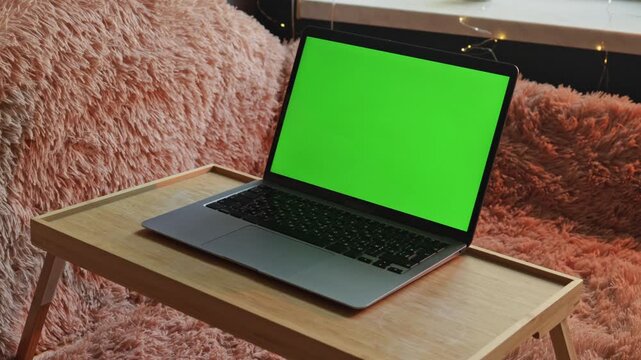 Laptop with green screen on a wooden tray on a fluffy blanket