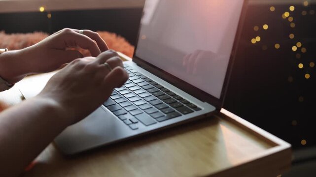 Close-up of hands typing on a laptop keyboard with warm bokeh lights in background