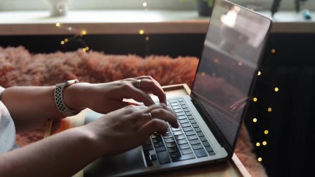 Close-up of hands typing on a laptop with cozy fairy lights in the background