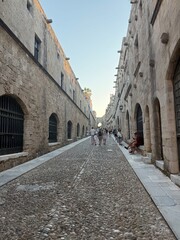 Fototapeta premium Handsome man in a burgundy linen shirt posing near the Palace of the Grand Master in Rhodes Old Town, medieval stone walls, Greek island, golden hour, elegant travel lifestyle