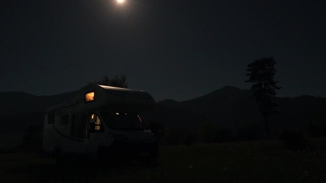 Luminous full moon ascending in the night sky over a camper van parked in a serene mountain landscape, with warm lights glowing from inside, suggesting a peaceful and adventurous getaway time lapse