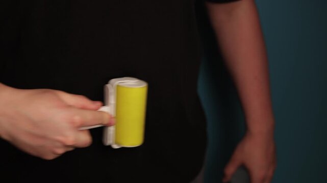 Person using a sticky lint roller to clean black clothing surface