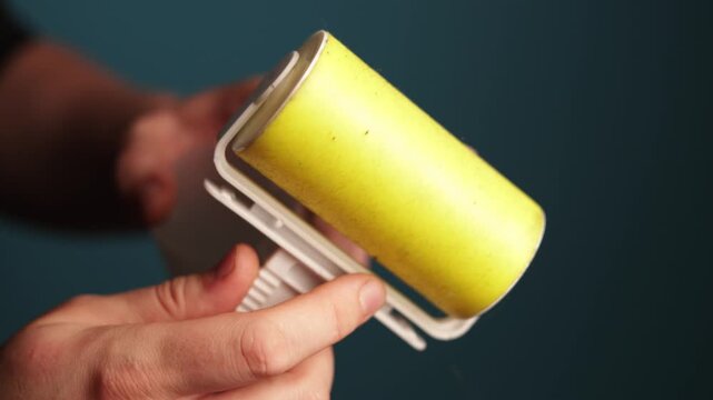 Close-up of hand using a sticky lint roller to pick up pet hair from clothing