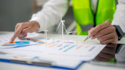 Close up engineer analyzing renewable wind turbine energy chart report with pen at office desk, sustainable green business strategy, ESG investment planning concept. © Ao Zaa Studio