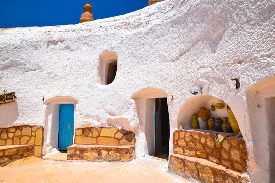 Interior courtyard of a traditional berber cave house with white walls, blue wooden door and orange stone bench in Sidi Meta near Matmata, Tunisia.