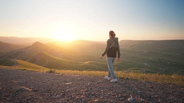 Young woman hiking along a dirt path on a hill overlooking a beautiful sea bay at sunset. Cinematic steadicam follow shot footage for active lifestyle, summer travel and freedom video.	