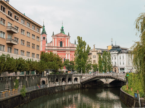 View of the Franciscan Church of the Annunciation and the iconic Triple Bridge spanning the Ljubljanica River in Ljubljana, Slovenia on an overcast day
