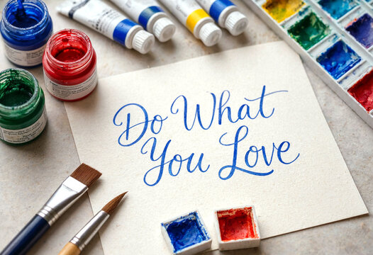 Handwritten do what you love quote surrounded by colorful paints and brushes on table