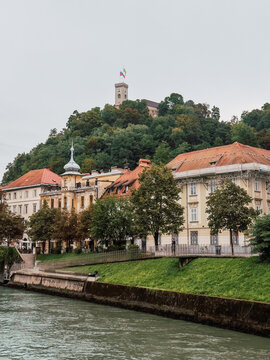 View of Ljubljana Castle rising above the riverside buildings and trees along the Ljubljanica River in the Slovenian capital.