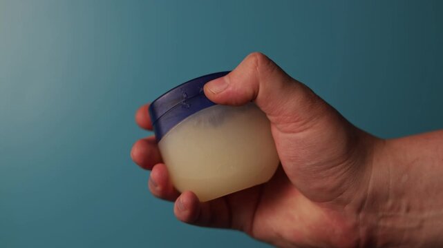 Hand applying petroleum jelly from a small blue container for skin care