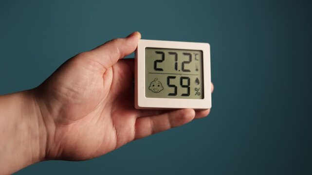 Close-up of hand holding digital thermometer and hygrometer displaying temperature and humidity