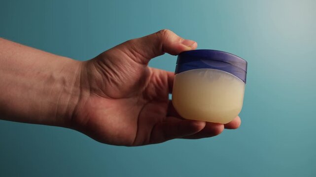 Hand holding petroleum jelly jar against a blue background