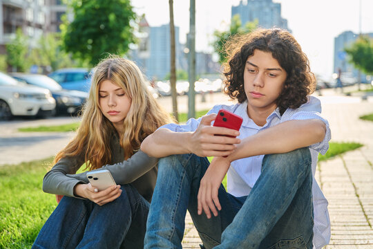 Teenage boy and girl sitting outside glued to smartphones