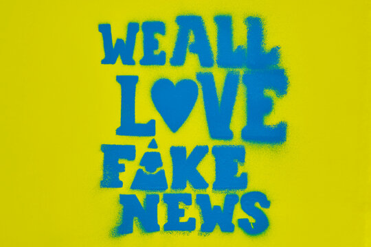 A bold statement with text we all love fake news in blue spray paint on a vibrant yellow surface conveys a critical message about misinformation and media.