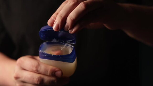 Close-up of hands opening and closing a petroleum jelly container