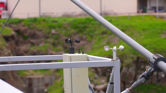 Two anemometers, a cup type and a vane type, spinning rapidly as they measure wind speed and direction at a meteorological station with a natural, grassy background