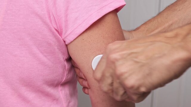 Man applying glucose monitoring sensor on woman arm with medical device