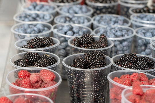 Ripe blackberries and other berries in plastic containers are displayed at a fruit stall in the market.
