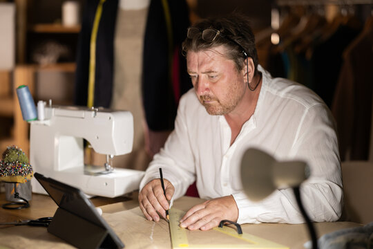 Middle-aged male dressmaker drawing on paper watching video-course
