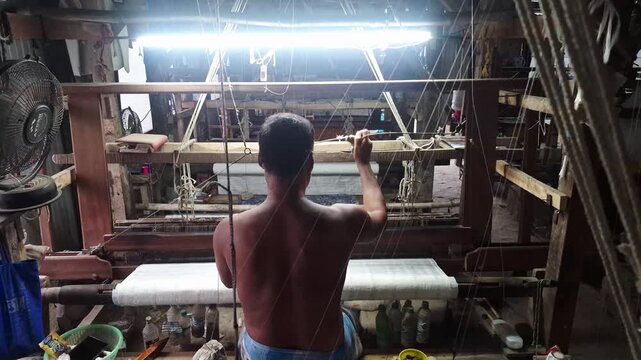4k 120 fps slow motion video of a handloom weaver in India working in his loom.	