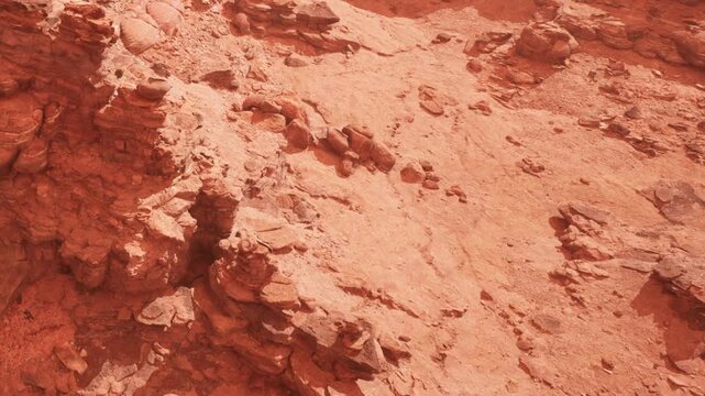 Rocks and soil in a dry desert area. The terrain is mostly barren, with various rock formations. The sunlight casts shadows on the ground.
