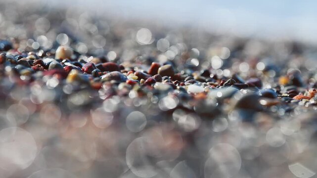 Multicolored pebbles scattered on bright sea shore with sparkling light reflections