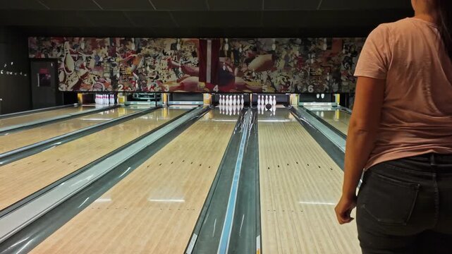 A person in a pink shirt bowls on an indoor lane with pins set up and vibrant wall art in the background at a bowling alley in Jelgava Latvia.
