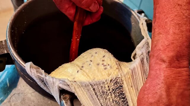 Hand stirring homemade cheese curds in a pot covered with cheesecloth in a kitchen in Cesis, Latvia during summer solstice.