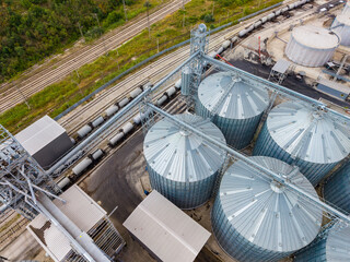 Grain storage facility near railway tracks with multiple silos and loading equipment during daytime © DSMT