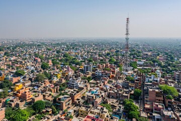 Naklejka premium Aerial view of dense urban settlement with prominent telecommunications tower rising above clustered buildings.