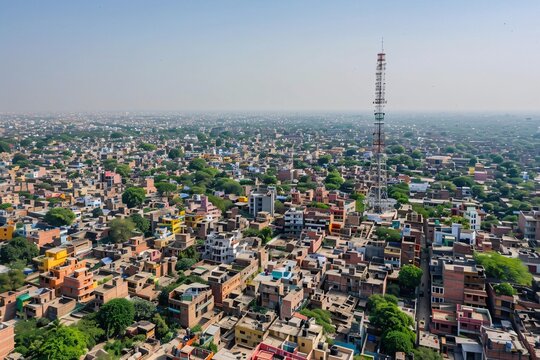 Aerial view of dense urban settlement with prominent telecommunications tower rising above clustered buildings.