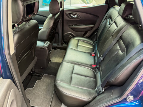 Interior view of a vehicle showing the backseat with leather seats and a center console at a parking location in daytime