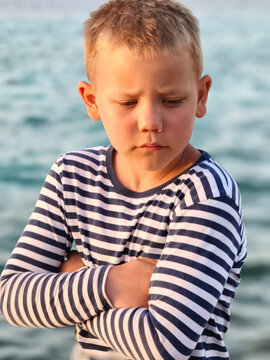 Young boy in a classic striped shirt stands confidently sea, his varied expressions capturing curiosity, contemplation, and carefree joy timeless portrait that tells story of childhood by shore.