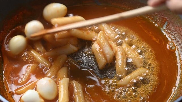Adding quail eggs to Korean Tteokbokki in a hot pan and stirring with a wooden spatula