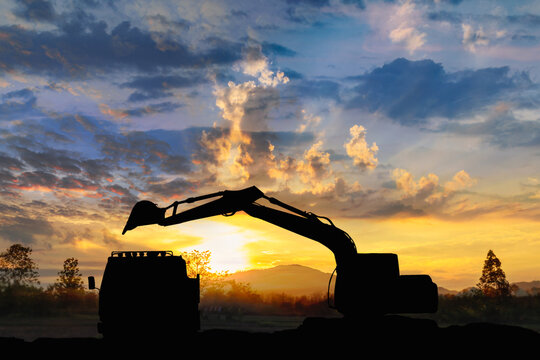 Crawler excavator silhouette digging the soil into a truck ,In the construction site on sunset  background.