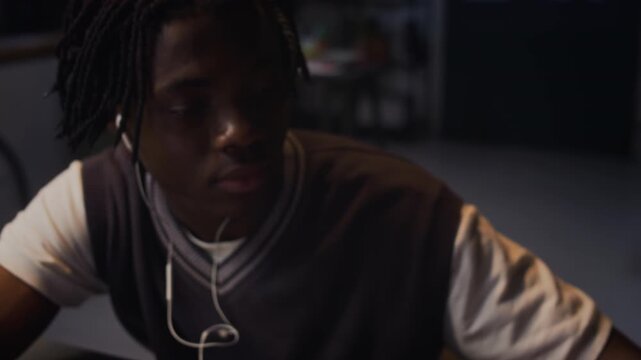 Young adult African American man checking 900 PM alarm on smartphone and working late at office desk while wearing earphones. Clip is ideal for corporate videos about overtime and burnout