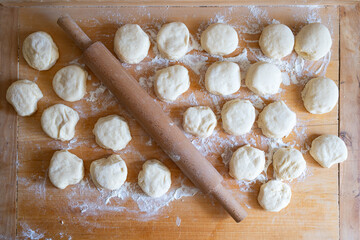 Flat lay top down view of raw dough portions and a wooden rolling pin spread across a floured baking board. © Octavian