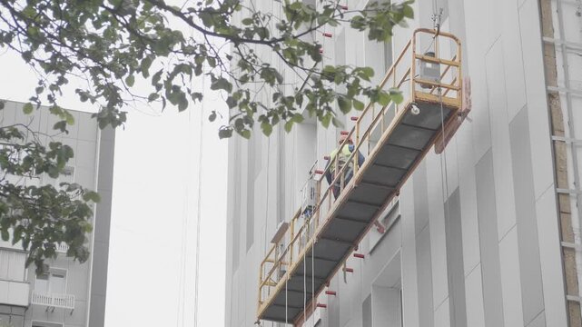 Construction workers on a suspended scaffolding platform working on the facade of a high-rise building