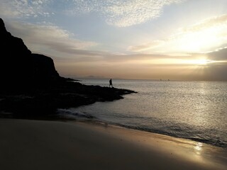 Person standing on volcanic rocks at sunset overlooking the Atlantic Ocean near Papagayo Beach, Lanzarote, Spain © Lilli Bähr