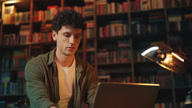 Young male scientist researching online material on laptop in a library