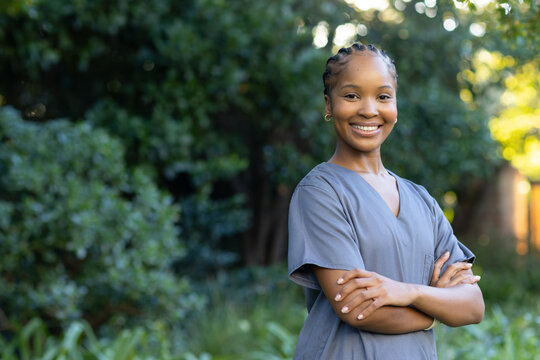 African American woman posing right in yard wearing gray scrubs hoops crossing arms, copy space