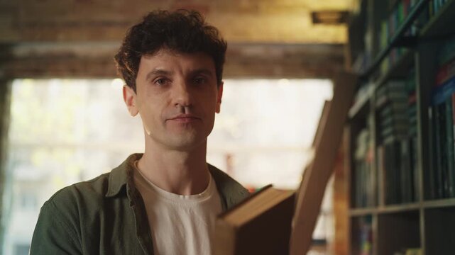 Portrait of happy young man holding a book in library, enjoying reading