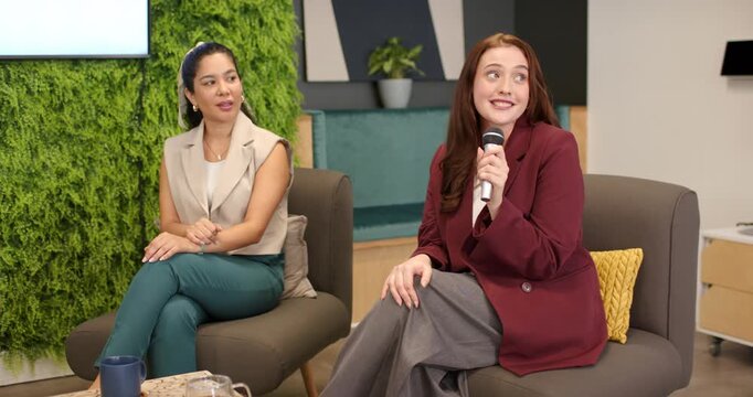 Female panelists holding microphones and discussing AI in office lounge being prompted by slide