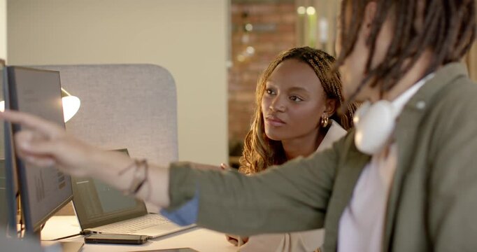 Diverse coworkers reviewing designs at desk, man pointing at monitors while woman giving input