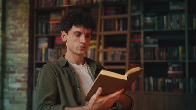 Concentrated young man reading a book in library, doing academic research