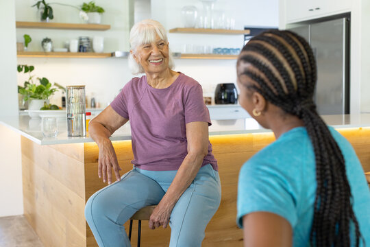Diverse female friends with Senior woman chatting at home kitchen island with pitcher glass shelves