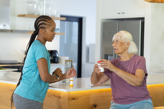 Diverse senior and adult women discussing medication at kitchen island holding medication container