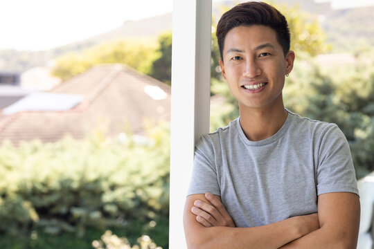Mid adult Asian man leaning on porch post, smiling, wearing gray tee, hoop earring, copy space