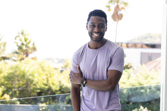 Man standing on glass balcony smiling toward camera while wearing light purple T-shirt and watch