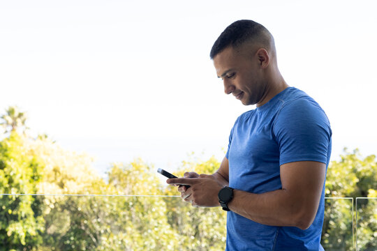 African man standing on glass balcony holding smartphone, wearing blue shirt and watch, copy space
